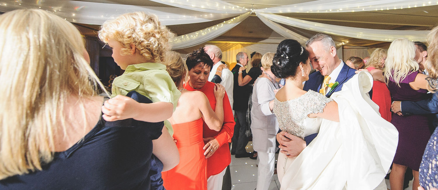 Romantic newlyweds embrance surrounded by party guests.