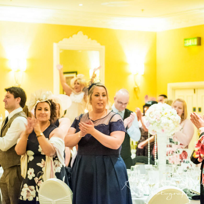 Guests stand dancing and clapping at tables during daytime show in south wales.