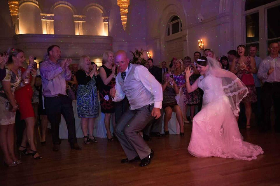 Clapping guests encircle bride and father dancing the locomotion at wedding party near bristol.