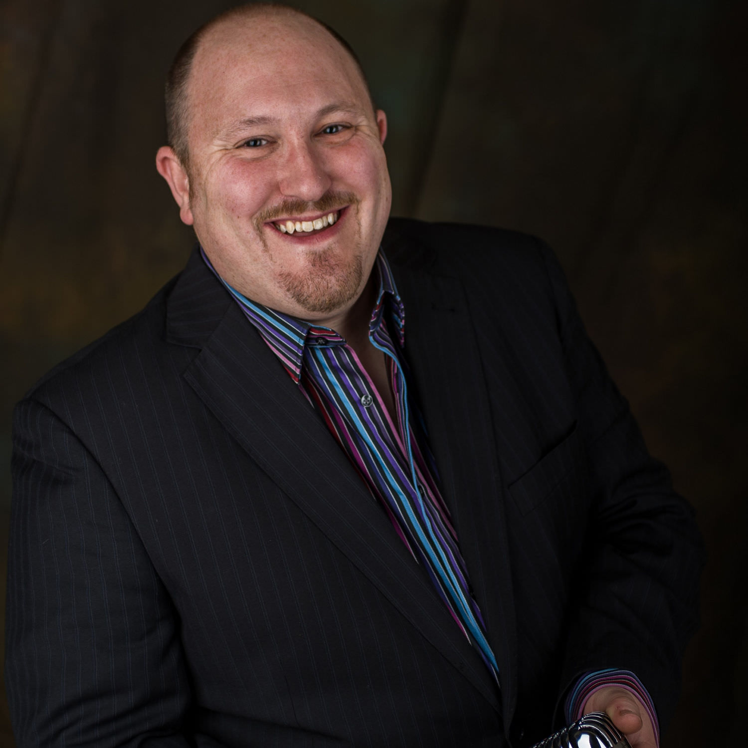 Jon paul wedding singer Bristol holding microphone and smiling in navy blue suit and rainbow striped shirt.