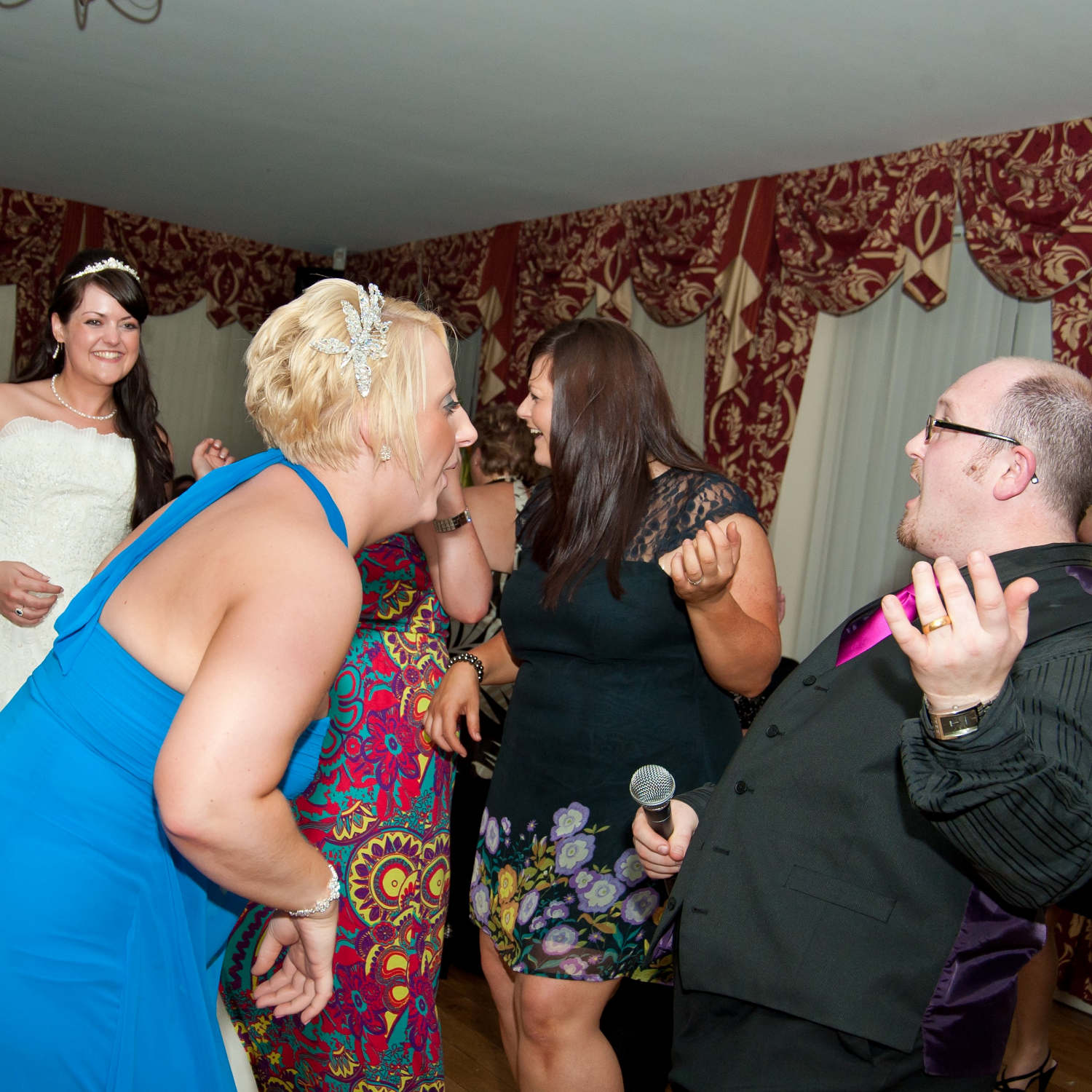 Bride grins in background while her friends surround jon paul wedding singer laughing as they play air guitars at Bristol wedding.